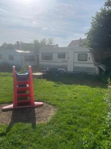 a red chair sitting in the grass next to an rv at Schlafen auf dem pferdehof einfach gehalten mit Kühlschrank in Duingen
