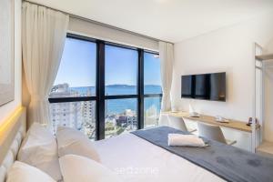 イタペマにあるMHFBs - Edifício Moderno c/ piscina vista mar em Itapemaのベッドルーム1室(ベッド1台、大きな窓のあるデスク付)