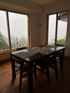 a table and chairs in a room with windows at Lifessenza Homestay in Khajjiar 