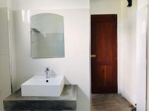 a bathroom with a white sink and a wooden door at Coastal Cloud Backpackers in Unawatuna