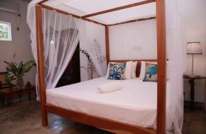 a bedroom with a canopy bed with white sheets and pillows at Coastal Cloud Backpackers in Unawatuna