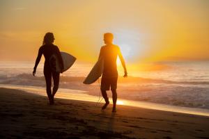 two people walking on the beach with their surfboards at Wellenkind Surfschool in La Pared