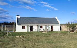 a white barn with a black roof in a field at Barn Owl Cottage in Riethuiskraal
