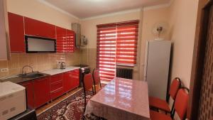 cocina con armarios rojos, mesa y nevera en Уютная квартира в Бухаре со всеми удобствами, en Bukhara