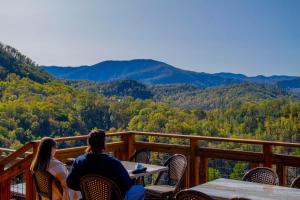 a man and woman sitting at a table on a deck overlooking the mountains at Stylish 1BR Free Attraction Tix Views! in Gatlinburg