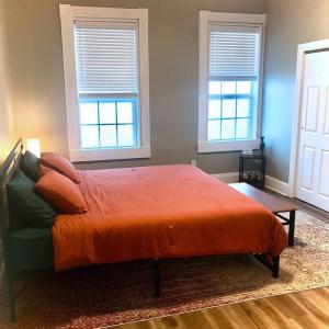 a bedroom with a bed with an orange blanket and two windows at Eco Friendly Home by Cincy w Office Space in Dayton