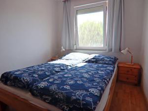 a bed with a blue comforter and a window at Strandhaus an der Wohlenberger Wiek in Hohenkirchen