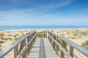 a wooden boardwalk to the beach with people on it at Enebrales Home in Punta Umbría