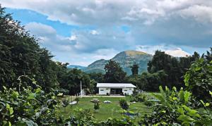 a white house in a field with mountains in the background at Takraw Rim Kwae ตะคร้อริมแคว in Ban Pong Pat