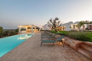 a row of lounge chairs next to a swimming pool at Tenuta PANORAMICAPULIA - Luxury Masseria Ostuni in Ostuni