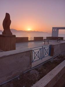 a sunset over the ocean with a statue and benches at Senza Pensieri Holiday Home in Balestrate