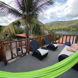 a hammock on a deck with chairs and a palm tree at Casa Temporada Waldemar Damasceno - Beira Rio com piscina in Piranhas