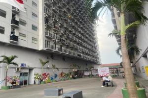 a building with a palm tree and people sitting on a bench at Hotel O Grand Asia Afrika Apartment By Qr Property in Bandung