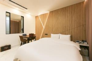 Un dormitorio con una cama blanca y una pared de madera. en Daegu Hotel Series Lions Park, en Daegu