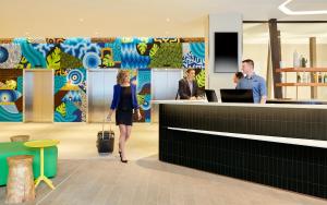 Una mujer con una maleta pasando por un mostrador en Holiday Inn Express Adelaide City Centre by IHG, en Adelaida