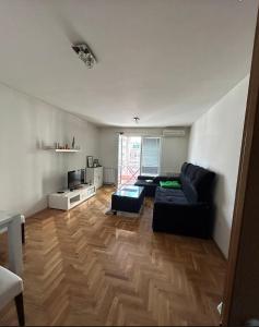 ein Wohnzimmer mit einer schwarzen Couch und einem Holzboden in der Unterkunft Apartman SARA in Sarajevo