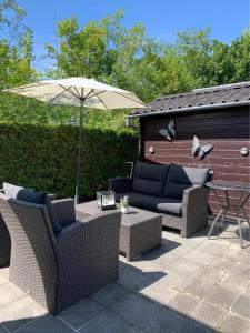 un patio con due divani e un ombrellone di Verzorgd chalet in de Betuwe op park met natuurbad a Beesd Altre 4 foto
