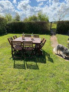 a wooden table and chairs with a dog sniffing the grass at Samphire Cottage in Stiffkey
