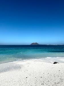 a white beach with blue water and a mountain in the background at Amazing villa by the beach with private pool in Corralejo