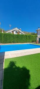 a blue swimming pool with green grass in front of a house at Casa Rural Fuente del Céfano in Arroyo Frio