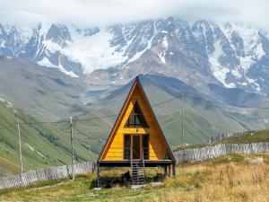 uma pequena casa numa colina com montanhas ao fundo em 4 Views Of Ushguli em Ushguli