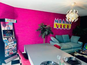 a room with a pink wall with a table and a couch at Capsule Miami Vice - Jacuzzi - Billard - Ecran cinéma & Netflix - Ping-Pong - Nintendo & Jeux- in Liévin
