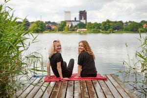 two women sitting on a wooden bench in front of a body of water at Danhostel Haderslev in Haderslev