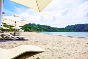 a beach with chairs and umbrellas and the water at PICO DE LORO Pool Accessible CAROLA 2 Bedroom Units by SEE Condominiums in Nasugbu