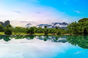 a pool of water with trees and clouds in the background at Lisha Garden Resort Hotel in Vang Vieng