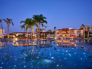 a pool at night with palm trees and buildings at Port Royal Villas and Spa - Adults Only in Kolymbia