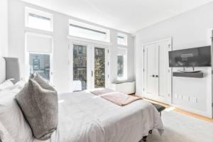 a white bedroom with a bed and a flat screen tv at Luxe Studio w Juliet Balcony in Upper East in New York