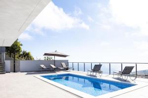 a swimming pool on a patio with chairs and an umbrella at Vila Indigo in Arco da Calheta