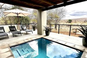 a swimming pool with two chairs and an umbrella at Bateleur Kruger Lodge in Marloth Park
