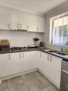 a white kitchen with white cabinets and a sink at Lbarza Charming & Convenient 3BR Home close to Hospitals & Sporting Grounds in Shepparton