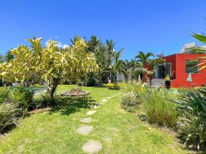 a garden with a red house and trees and grass at Domaine Putu Bali - Havre de paix & Piscine Lagon in Petit Raffray