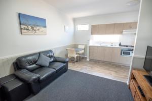 a living room with a black leather couch and a kitchen at Esperance Bay Holiday Park in Esperance