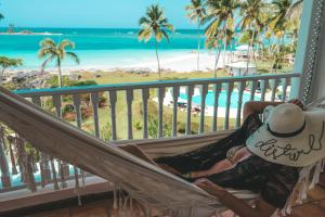Una mujer sentada en una hamaca en un balcón con vistas a la playa. en Hotel Villa Serena, en Las Galeras