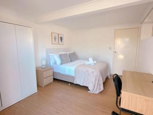 a white bedroom with a bed and a desk at Comfy unit near Garden City Westfield Street Parking in Brisbane