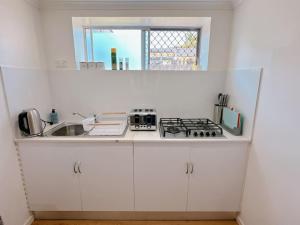 a white kitchen with a stove and a sink at Comfy unit near Garden City Westfield Street Parking in Brisbane