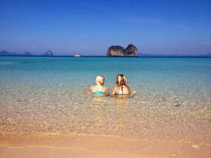 two girls are sitting in the water on the beach at Thanya Beach Resort - SHA Plus in Ko Ngai