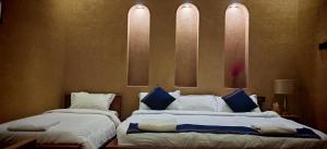 una camera con 2 letti con lenzuola bianche e cuscini blu di Omani Guest House نزل البيت العماني a Nizwa