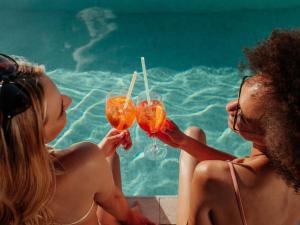 two women sitting next to a swimming pool holding drinks at WakakaPackers in Kuala Lumpur