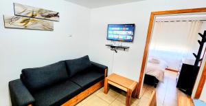 Una sala de estar con un sofá negro y un televisor. en Belgrano 555, en San Martín de los Andes