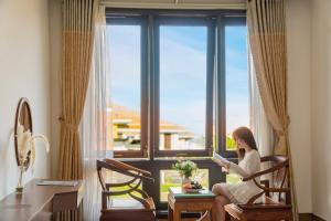 a woman sitting in a chair looking out of a window at SeaColor Beachstay Danang Hotel by Haviland in Da Nang