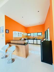 an orange kitchen with two stools and a counter at ชิลชิลขนอมพูลวิลลา in Ban Thong Ching