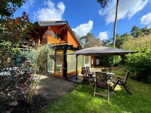 a house with a table and chairs and an umbrella at Houten chalet/bungalow in het bos, sauna, jacuzzi in Meijel