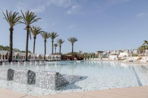 a large swimming pool with palm trees and umbrellas at Hard Rock Hotel Ibiza in Playa d'en Bossa