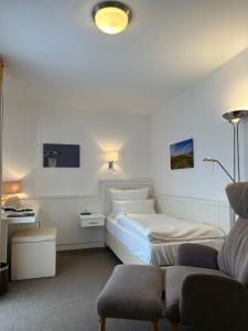 a white bedroom with a bed and a chair at Romantik Hotel Achterdiek in Juist