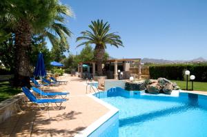 a swimming pool with blue chairs and palm trees at Alianthos Suites in Tersanas