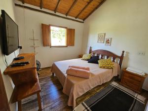 a bedroom with a bed with a desk and a television at Chalés Vila Carrancas - Ao lado do centro com piscina, cozinha completa e muita tranquilidade in Carrancas +102 photos